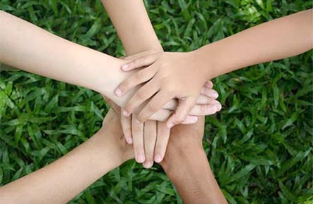 Image of five arms coming together with hands laid on top of one another