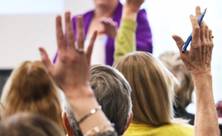 Image depicts a community networking event with a cropped in focus around hands being raised